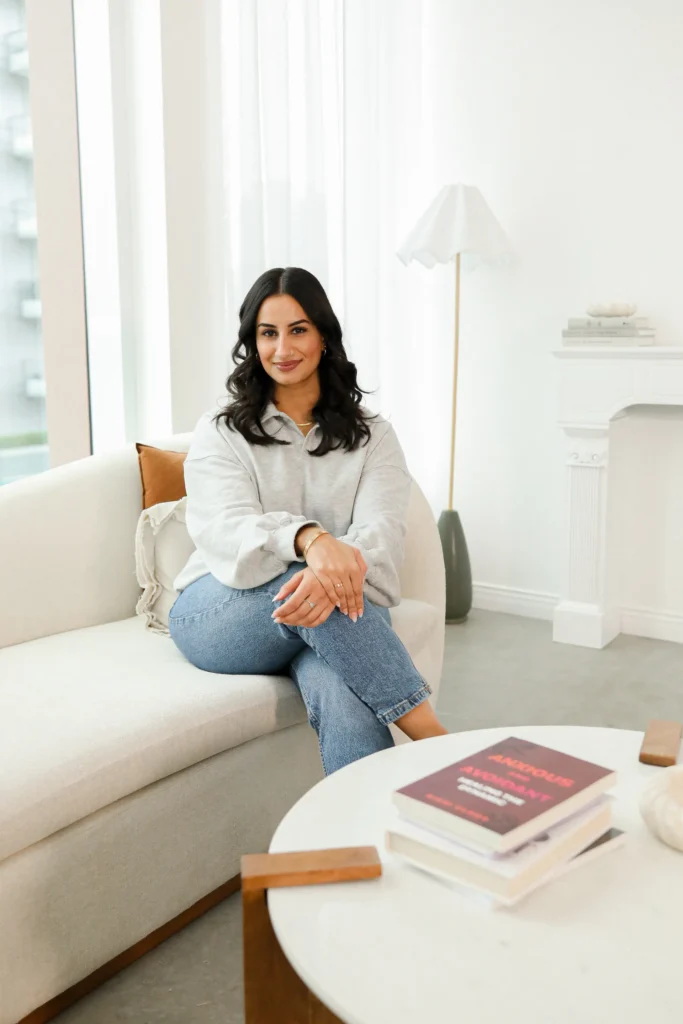 Natasha Wahi on a white couch, exemplifying professional and reflective clinical supervision for early-career therapists.